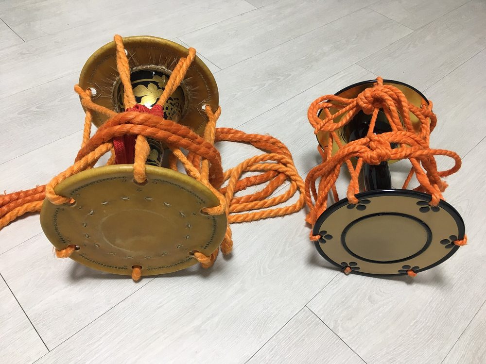 Two hourglass-shaped hand drums side by side, laced with cords